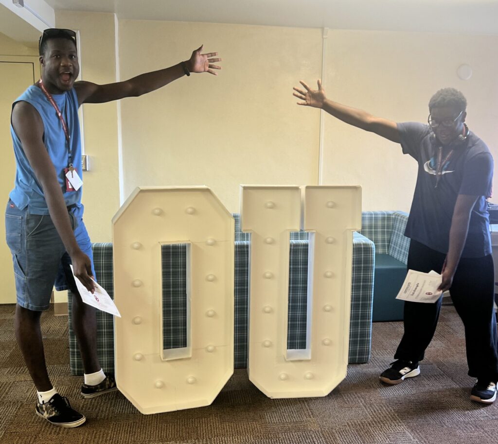 2 college students gesturing towards the oversized letters O.U.